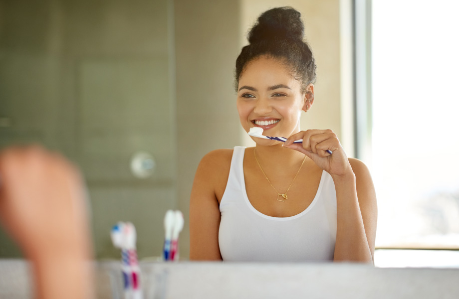 young woman brushing teeth in mirror