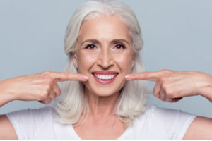 white haired woman pointing at her white smile with both fore fingers