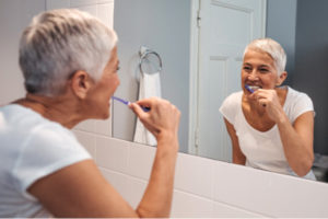 elderly woman brushing her teeth in front of the bathroom mirror