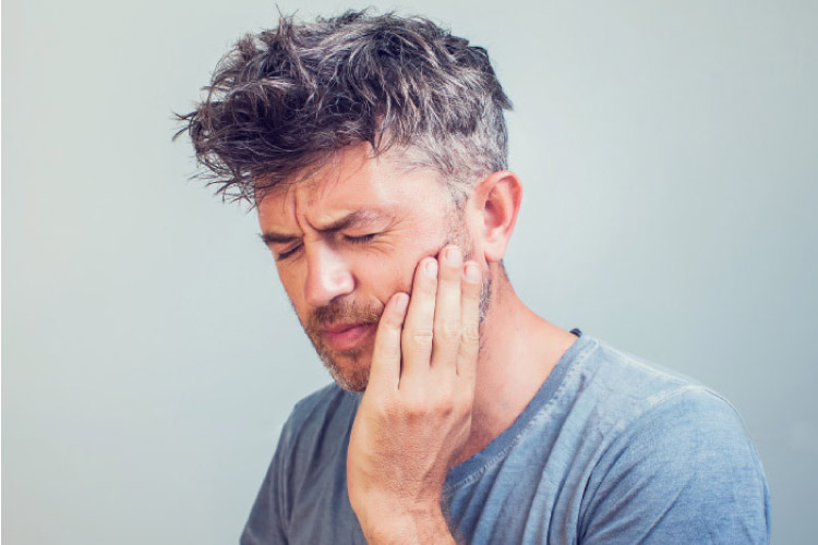 man holding his jaw in pain from a tooth that needs extracting