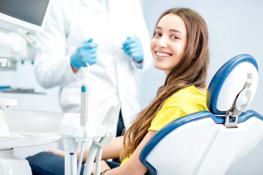 Brunette woman in a yellow shirt smiles while sitting in the dentist chair for preventive dental care