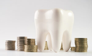 A tooth next to piles of coins to symbolize the savings from an affordable in-office dental savers plan