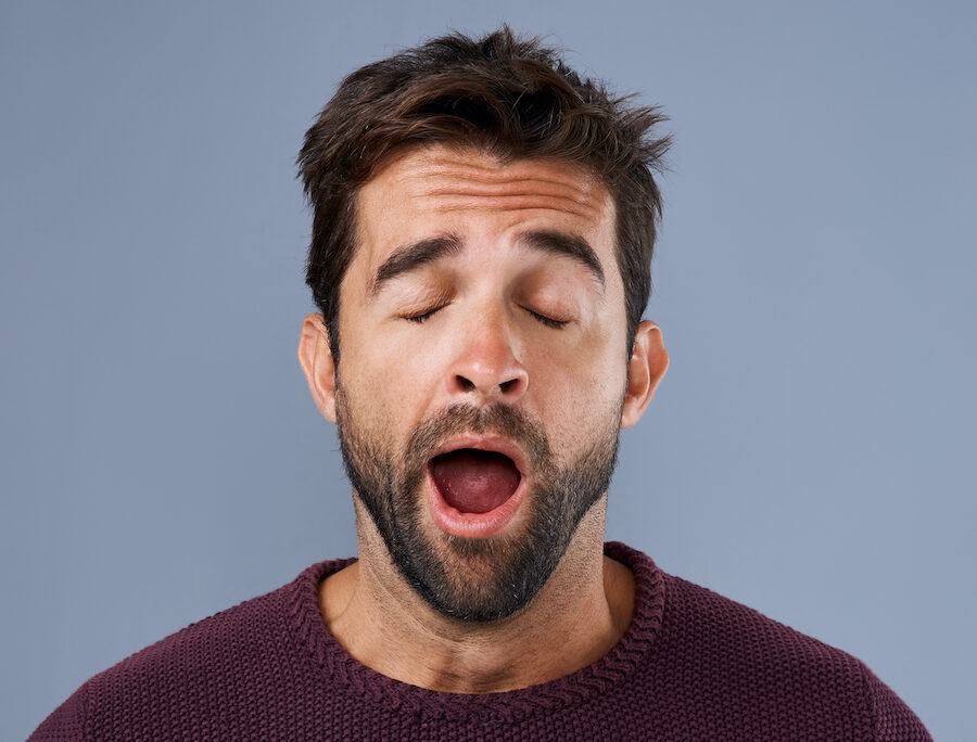 Brunette man in a maroon shirt yawns due to daytime sleepiness from bad sleep