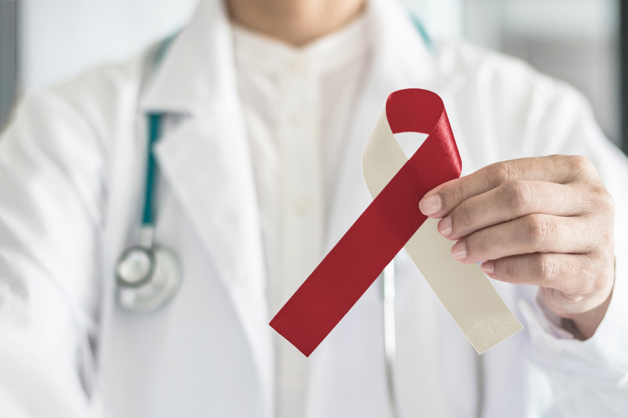 A dentist holds a cream and red ribbon for oral cancer awareness