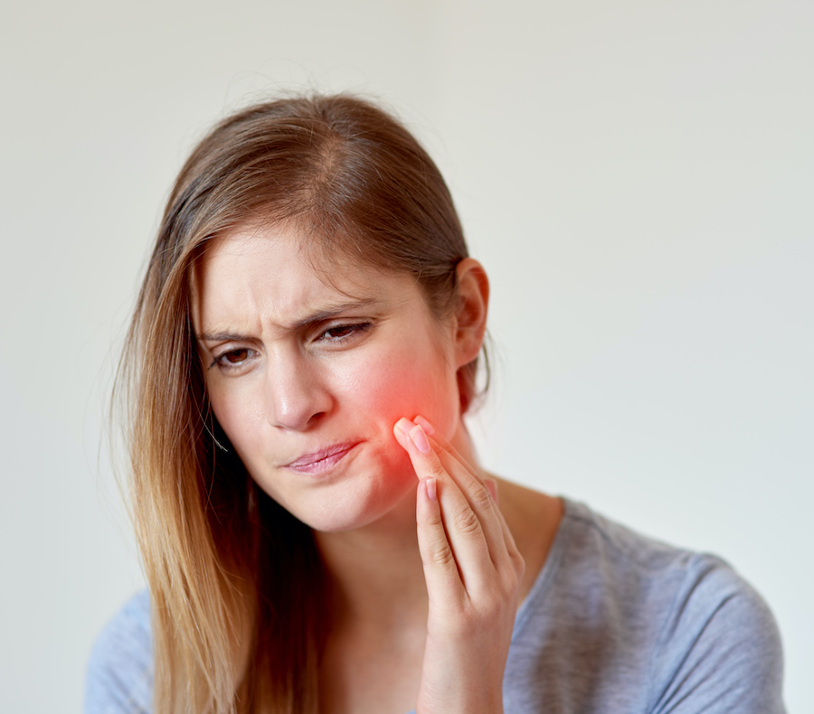 Blonde woman cringes in pain and touches an artificially red hot spot on her cheek that indicates she has a dry socket