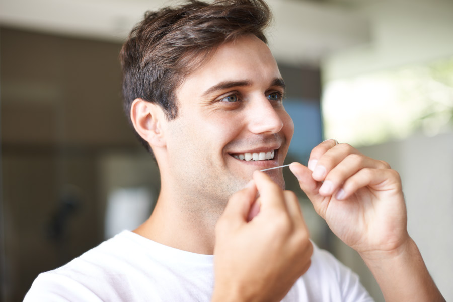 Brunette man in a white t-shirt smiles as he flosses his teeth